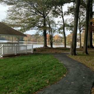 A peaceful park scene with a lake, trees, and a winding path leading to a gazebo.