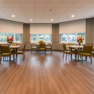 An empty dining room with neatly arranged tables and chairs, featuring large windows and flower centerpieces.