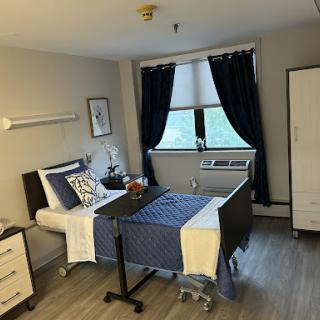 A tidy hospital room equipped for patient care, featuring a bed, wardrobe, and large window.