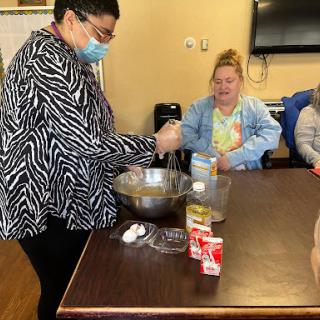 A group cooking session where a participant demonstrates mixing ingredients while others observe.