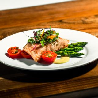 A gourmet dish featuring grilled salmon served with asparagus and cherry tomatoes, garnished with fresh herbs.