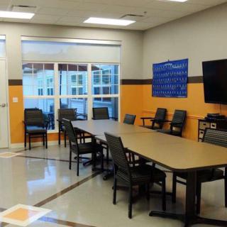 A modern conference room with a large meeting table and chairs, featuring a television and a spacious window.