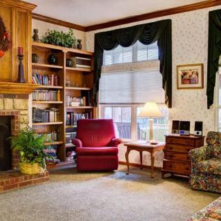 A cozy traditional living room with a fireplace, bookshelves, and a comfortable armchair near the window.