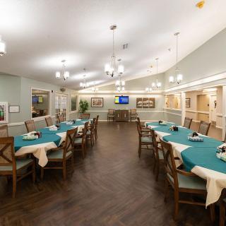 A spacious dining area with multiple tables and chairs, featuring elegant lighting and wooden flooring.