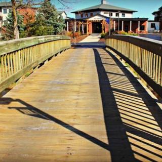 A wooden bridge leading to a building, casting long shadows on a sunny day.