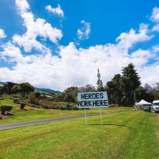 A scenic outdoor landscape featuring a sign on a grassy field under a blue sky with clouds.