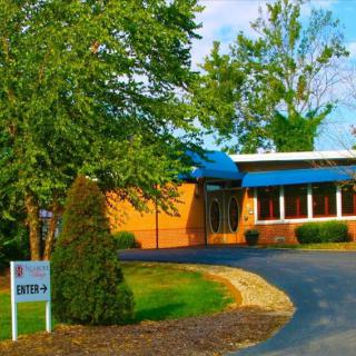 A commercial building with a blue awning surrounded by trees and landscaping on a clear day.