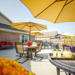A sunny patio with tables and chairs under yellow umbrellas, decorated with vibrant flowers.