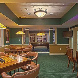 A cozy recreation room featuring a pool table, chess board, and seating area with warm lighting.