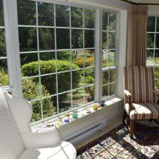 A sunlit room with comfortable chairs and a view of lush greenery outside the large windows.