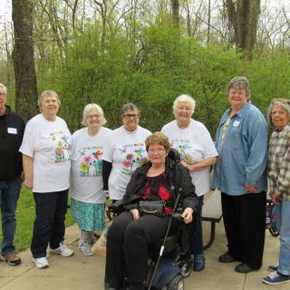A group of adults posing for a photo outdoors in a park, with one individual seated in a wheelchair.