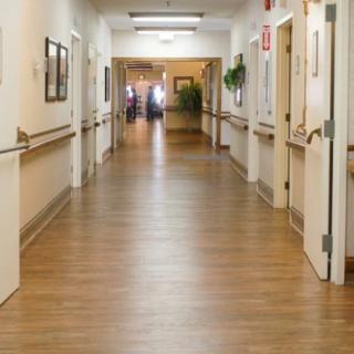 A hospital corridor with handrails and several doors along the hallway.