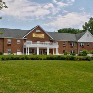 A two-story brick building with a manicured lawn and cloudy sky.