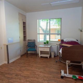 A well-lit room featuring a hospital bed, chair, and storage shelves with a view of the outside through a window.