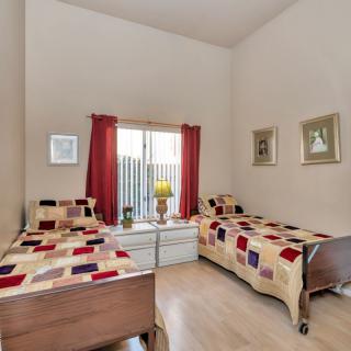 A cozy bedroom with twin beds featuring colorful quilted bedding, complemented by wall art and a central window with red curtains.