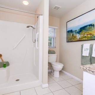 A clean bathroom with a shower, toilet, and sink, featuring decorative towels and artwork.