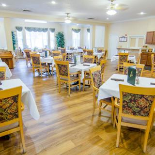 A bright and spacious dining room with neatly arranged tables and chairs, featuring wood flooring.