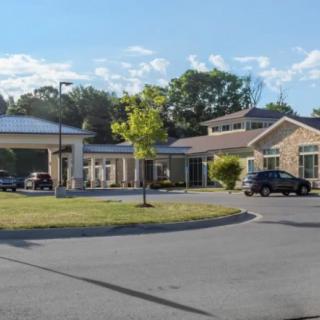 A view of a building with a driveway and parked cars on a clear day.