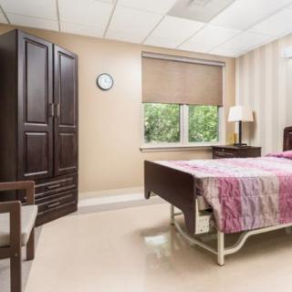 A tidy, well-lit hospital room with a bed, wardrobe, and window.