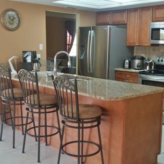 A modern kitchen with a granite countertop, bar stools, and stainless steel appliances.