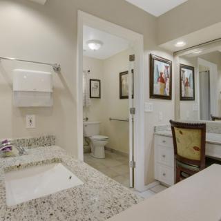 A modern bathroom with a granite countertop, sink, and mirror, featuring artwork and a view into the toilet area.