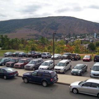 A parking lot filled with cars against a backdrop of hills and a cloudy sky.