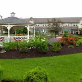 A beautiful garden with a white gazebo surrounded by lush greenery and colorful flowers in front of a large building.