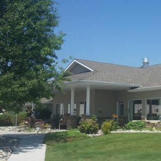 A suburban house with a spacious porch, surrounded by a well-maintained lawn and landscaping under a clear blue sky.