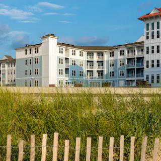 A modern coastal building surrounded by lush grass and a clear blue sky.