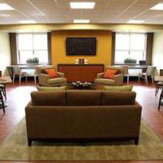 A modern lounge area with comfortable seating, a large TV, and ample natural light.