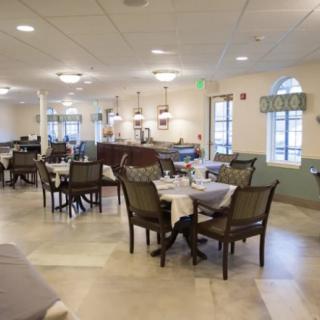 A spacious dining room with neatly arranged tables and chairs, featuring warm lighting and large windows.