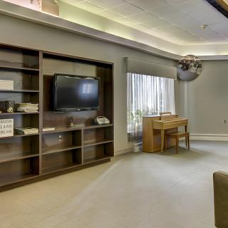 A modern living room featuring a television and shelves, with a piano by the window.