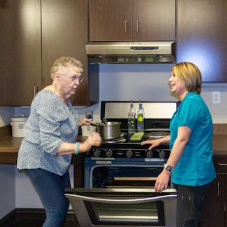 An elderly woman and a caregiver engage in conversation while preparing a meal in the kitchen.