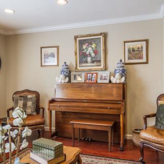 A cozy living room featuring a vintage piano surrounded by elegant chairs, decorated with artwork and family photographs.