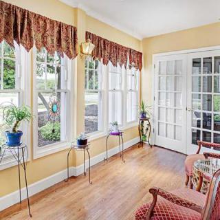 A bright sunroom with large windows, French doors, and potted plants on stands.