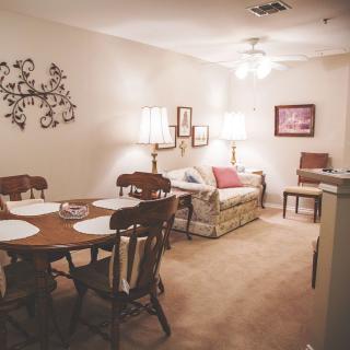 A cozy living and dining area with traditional furnishings, featuring a wooden dining table set and a comfortable sofa with lamps providing warm lighting.