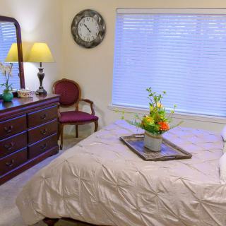 A cozy bedroom with elegant decor, featuring a bed with a flower arrangement, wooden dresser with mirror, and lamp.
