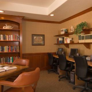 A cozy office space with bookshelves and computers, featuring wood furniture and comfortable chairs.