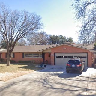 A suburban brick house with a driveway and car, surrounded by leafless trees.