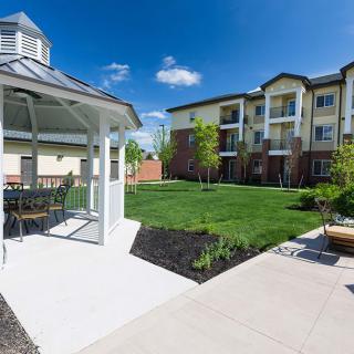 A well-maintained apartment complex featuring a gazebo, green lawn, and outdoor seating under a clear blue sky.