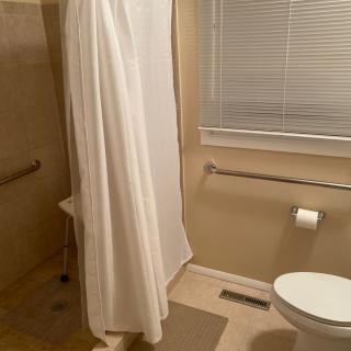 A clean bathroom with a shower, toilet, and window blind.