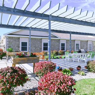 A peaceful patio with a pergola, surrounded by vibrant flowers and outdoor seating.