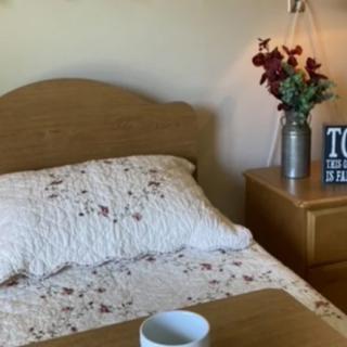 A cozy bedroom scene with a floral patterned bedspread, a vase of flowers on the nightstand, and a small decorative sign.