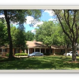 A suburban house surrounded by trees with cars parked in front.