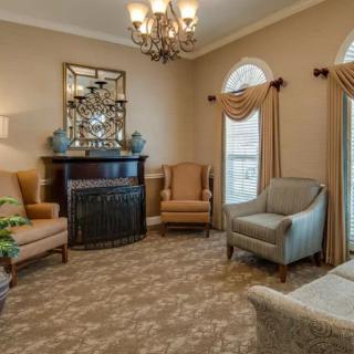 A cozy living room with traditional decor, featuring a chandelier, armchairs, and a fireplace.