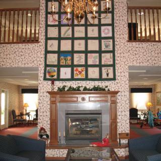 A cozy lobby featuring a fireplace, chandelier, and decorative quilt.
