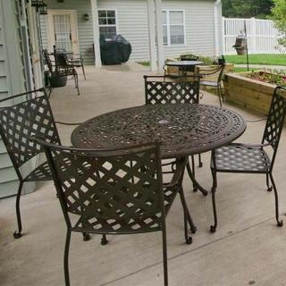 A metal patio table and chairs set on a concrete surface in an outdoor garden area.