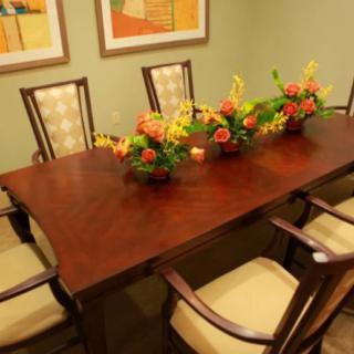 A dining room with a wooden table, surrounded by chairs and adorned with floral arrangements.