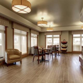 A spacious dining area with wooden floors, featuring several chairs and tables, large windows, and warm lighting.
