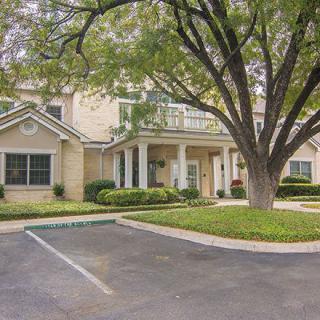 A residential building with a large tree and an adjacent parking lot.
